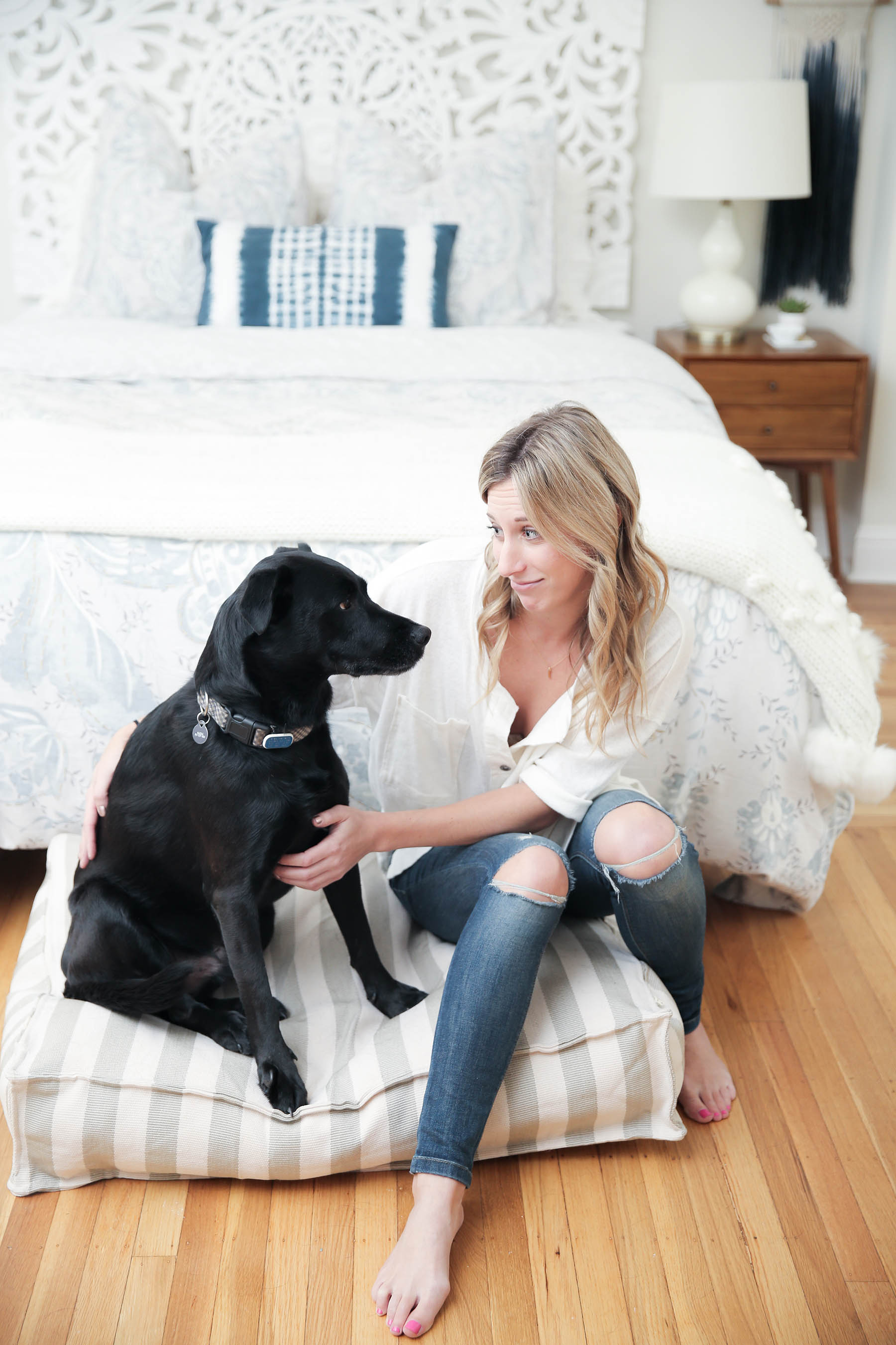 Amanda Holstein with her black lab dog Auggie in stylish boho bedroom