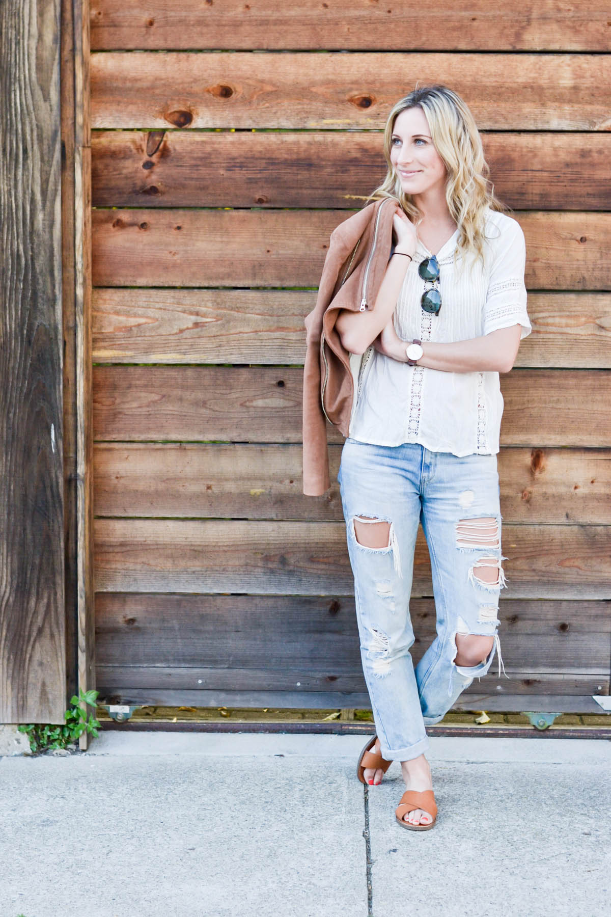 Amanda Holstein in revolve clothing white lace top, madewell sunglasses, brown suede moto jacket, ripped boyfriend jeans, distressed denim, and madewell slides brown leather sandals