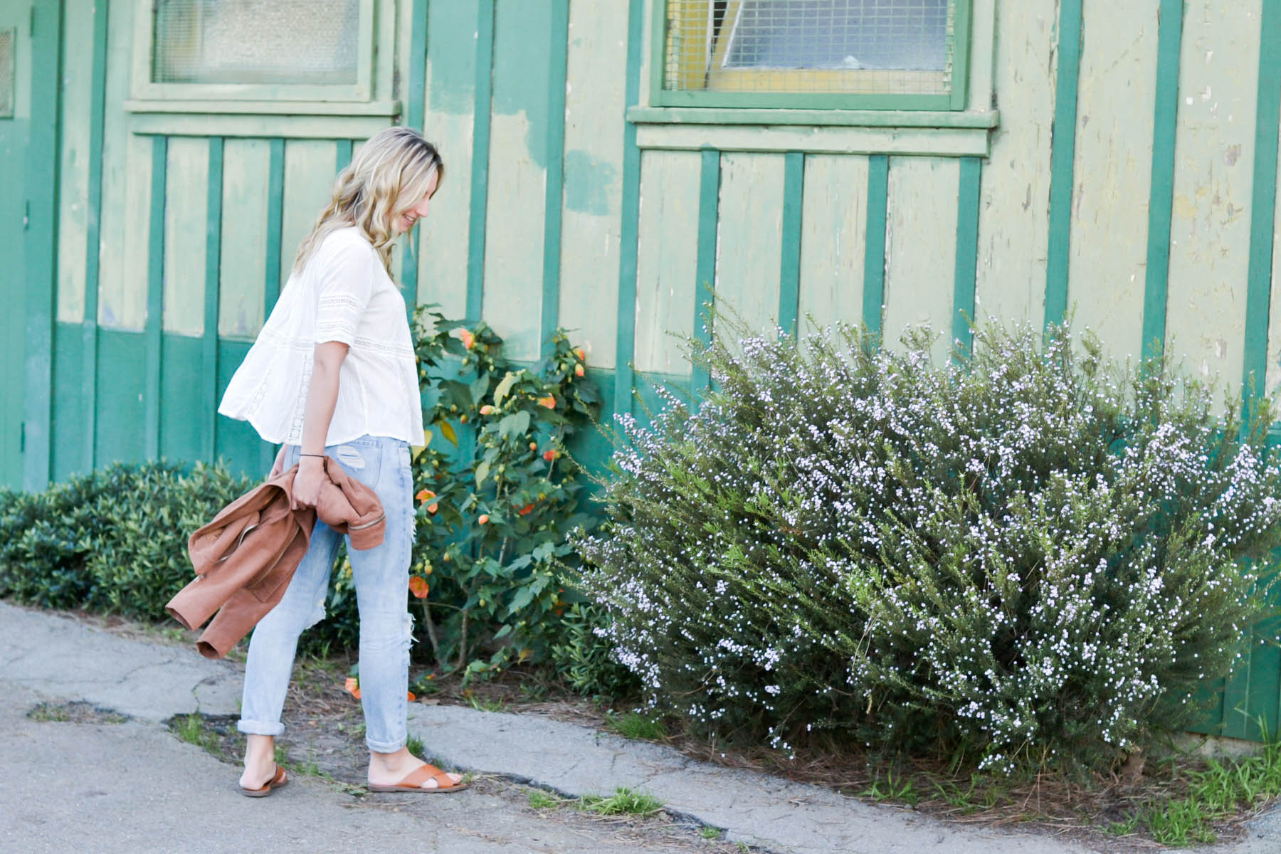 Amanda Holstein in revolve clothing white lace top, madewell sunglasses, brown suede moto jacket, ripped boyfriend jeans, distressed denim, and madewell slides brown leather sandals