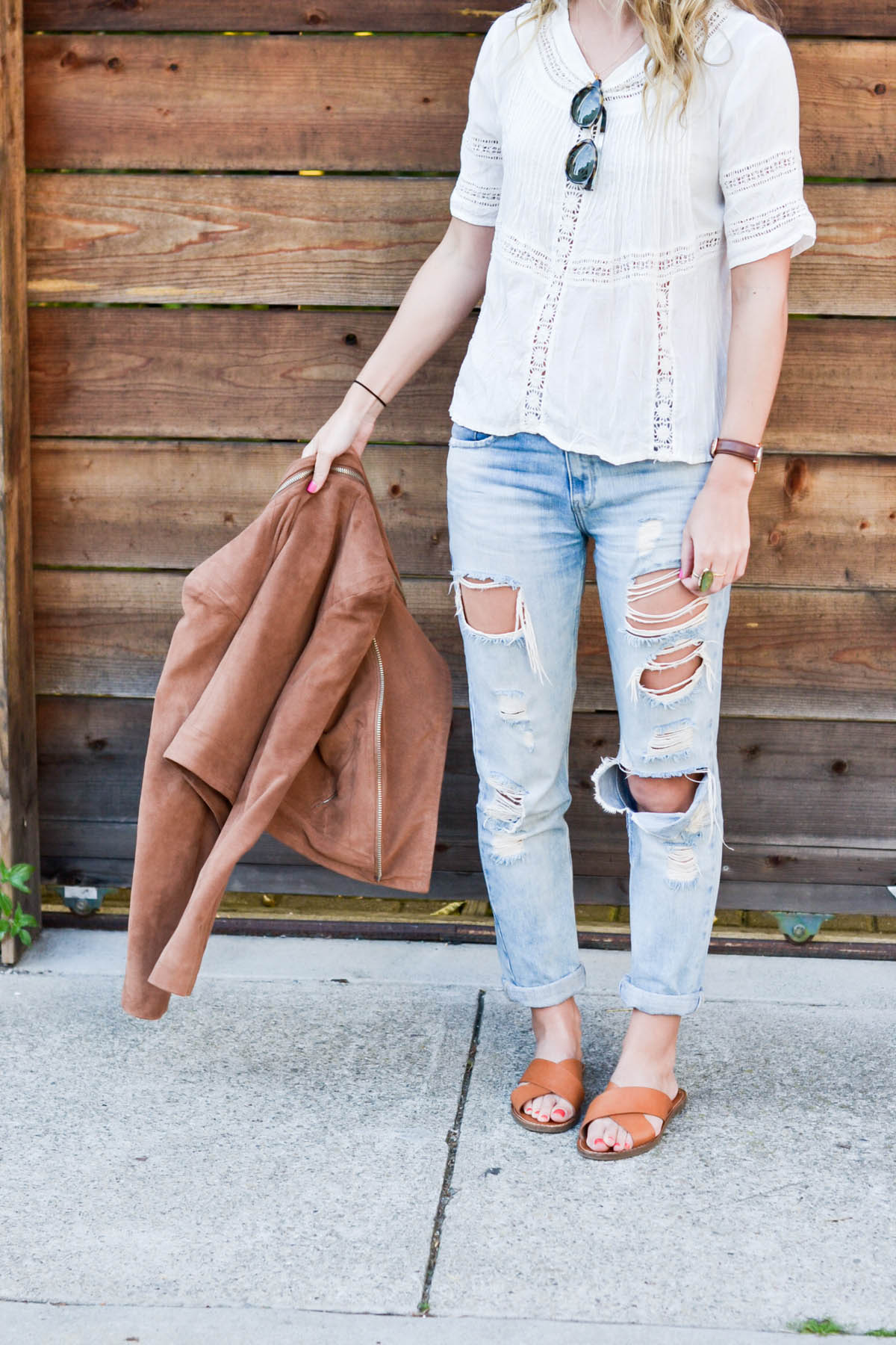 Amanda Holstein in revolve clothing white lace top, madewell sunglasses, brown suede moto jacket, ripped boyfriend jeans, distressed denim, and madewell slides brown leather sandals