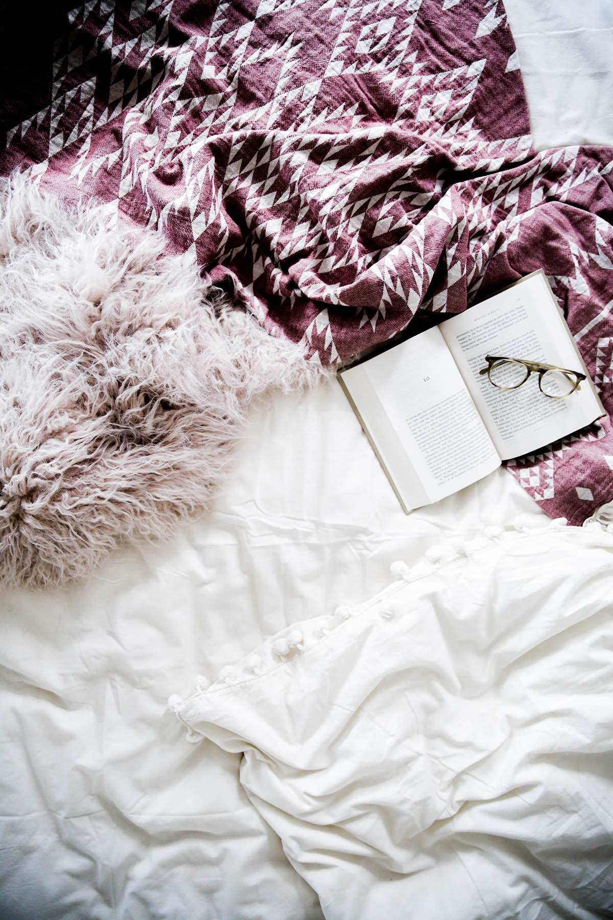 book and glasses in bohemian bed with Urban Outfitters Magical Thinking Pom-Fringe Duvet Cover and Faux Lamb Fur Throw Blanket