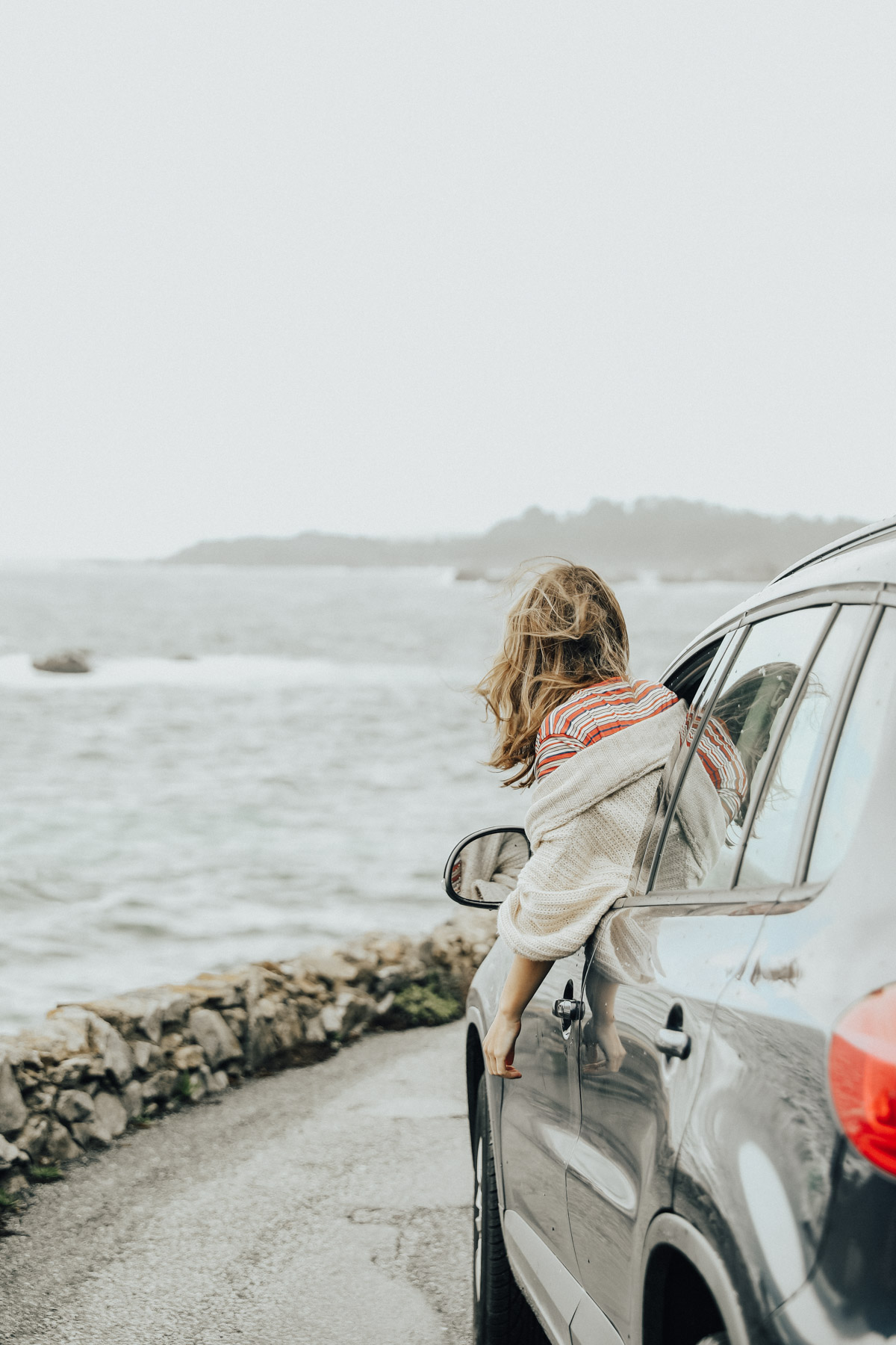girl hanging out of car on road trip with view of pacific coast
